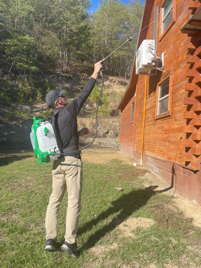 Pest X technician treating the exterior of a wooden cabin in Double Springs, Alabama.