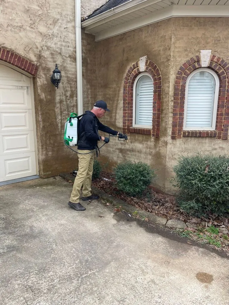 Pest X technician applying an exterior treatment to a home.