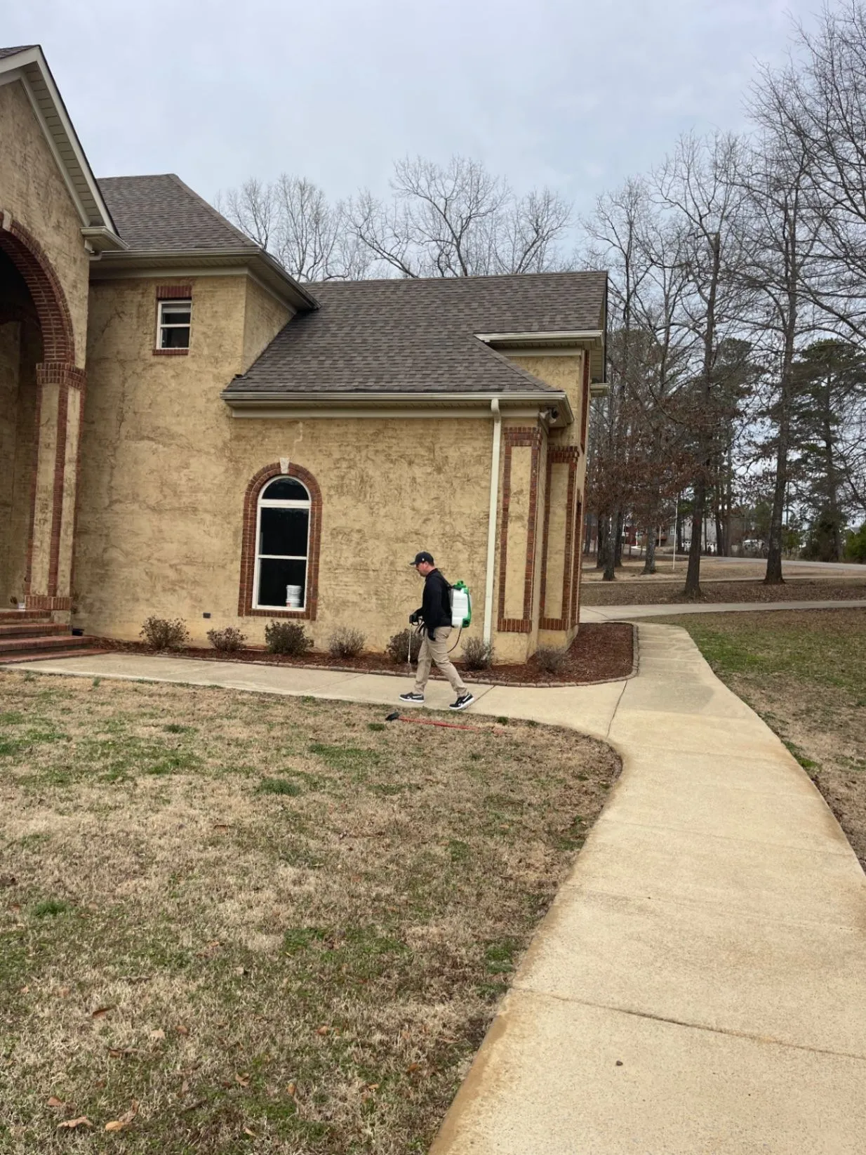 Pest X technician treating the exterior of a home with a backpack sprayer.