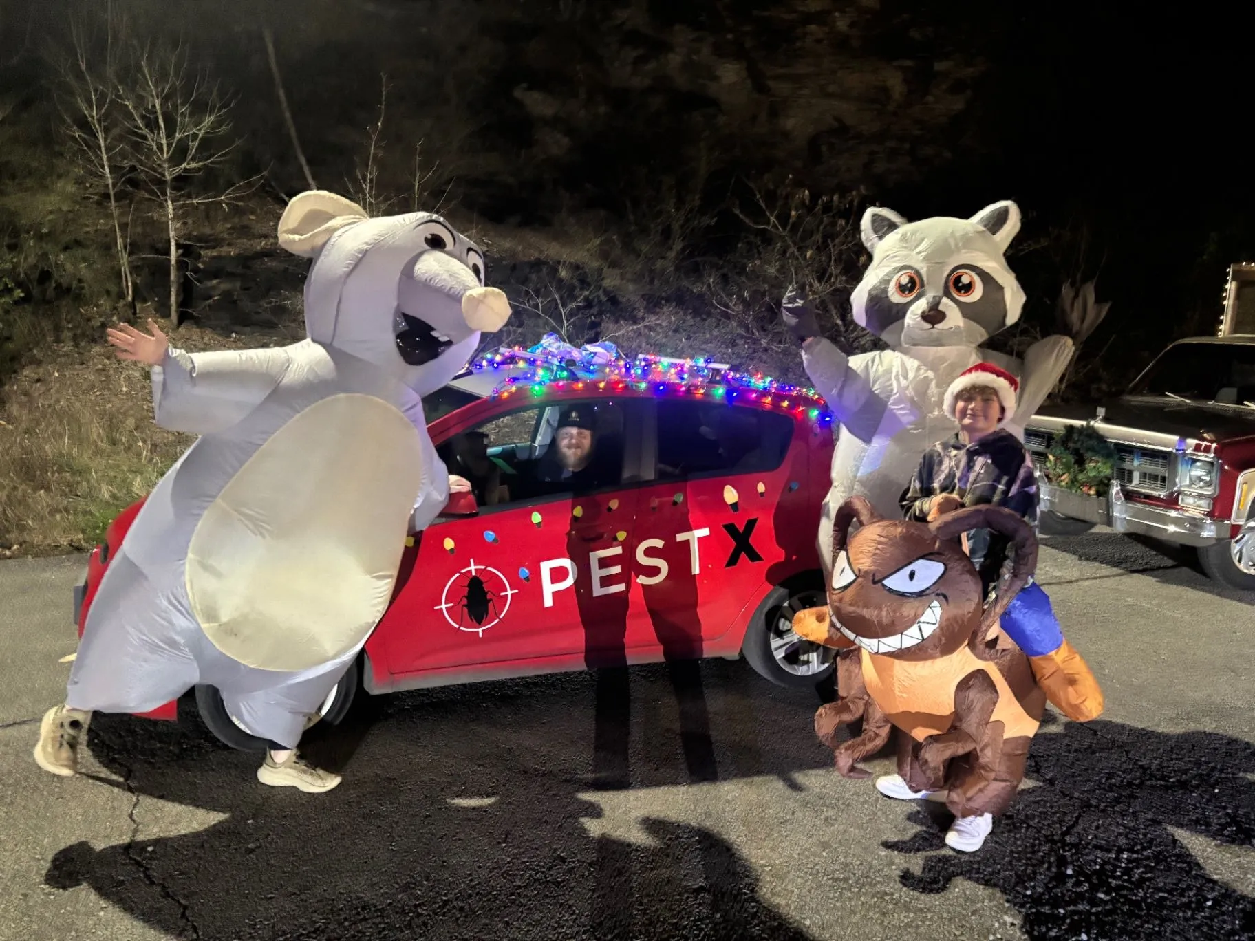 Pest X team members in costumes beside a decorated Pest X vehicle at a Christmas parade.